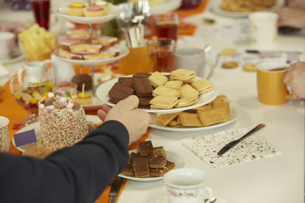 A hand reaches out holding a plate of bourbon biscuits and custard creams.