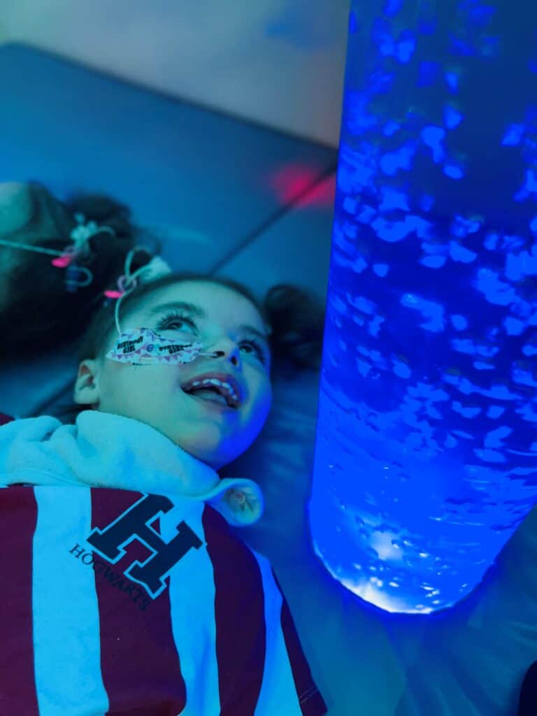Verity, a small girl, lying on the ground looking up at the blue light of a sensory tube.