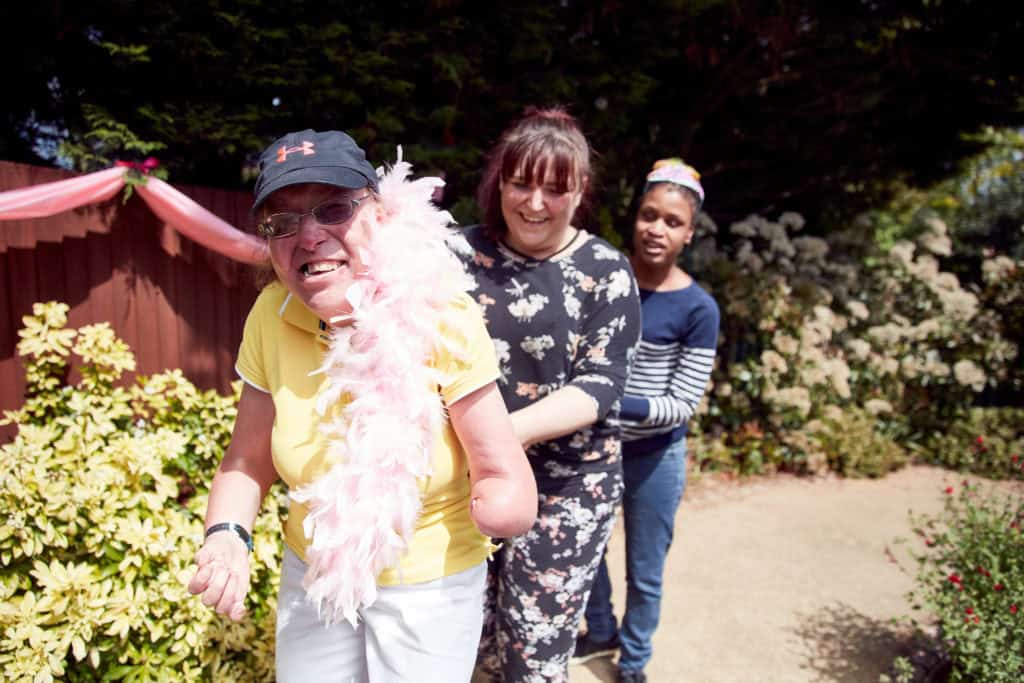 Three woman dancing in a line on a sunny day. The lady in the front is wearing a pink sash