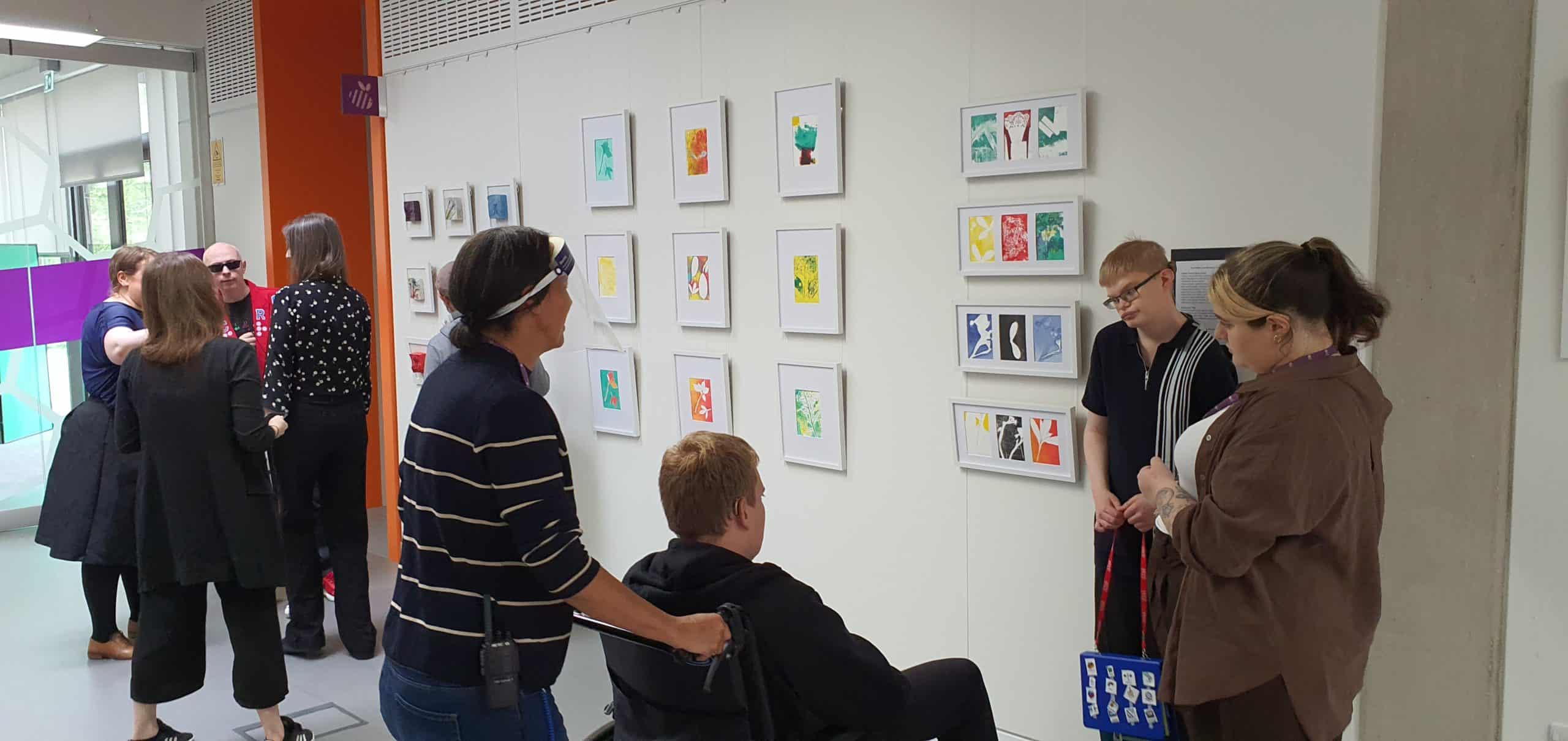 A woman guiding a man in a wheelchair viewing textured artworks hung on a wall