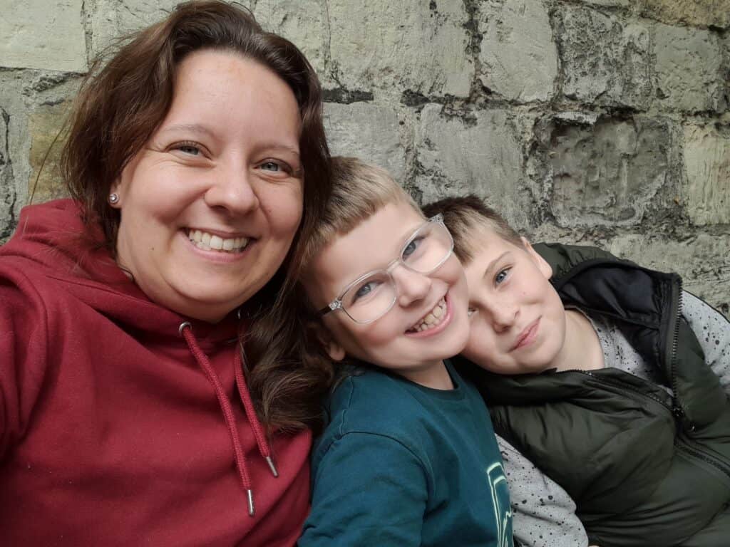 Catherine, a white woman with brown hair, smiling with her two young sons, Marshall and Reuben.