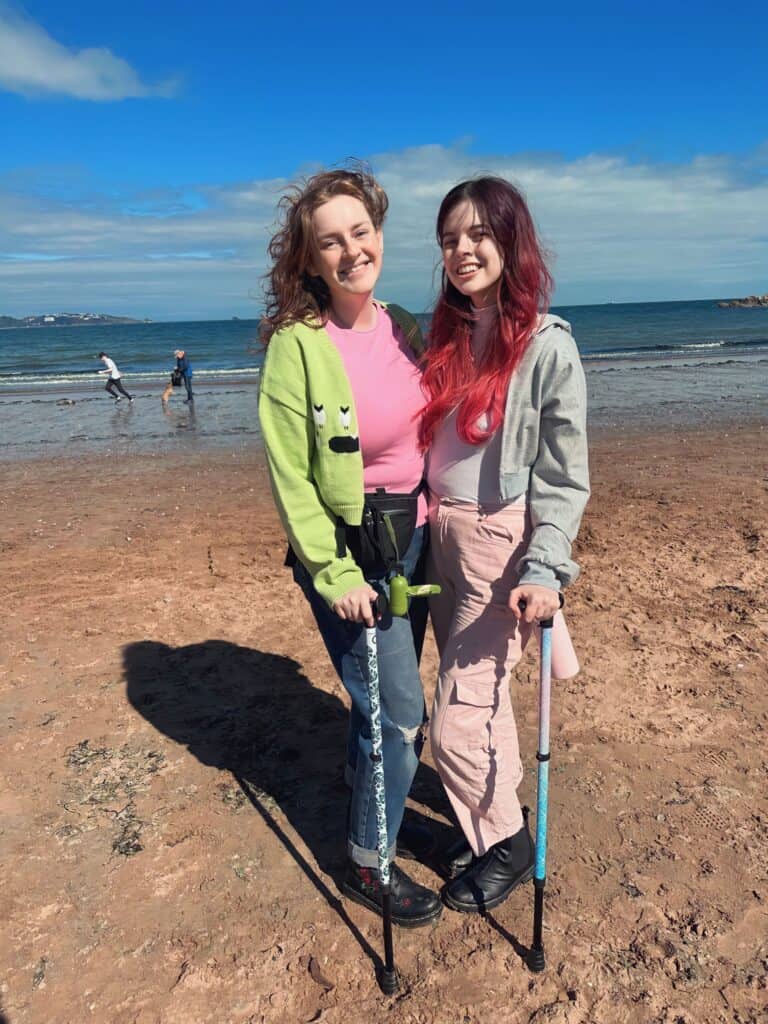 Jeffie and Ru standing on the beach with their walking sticks, both smiling for the camera.