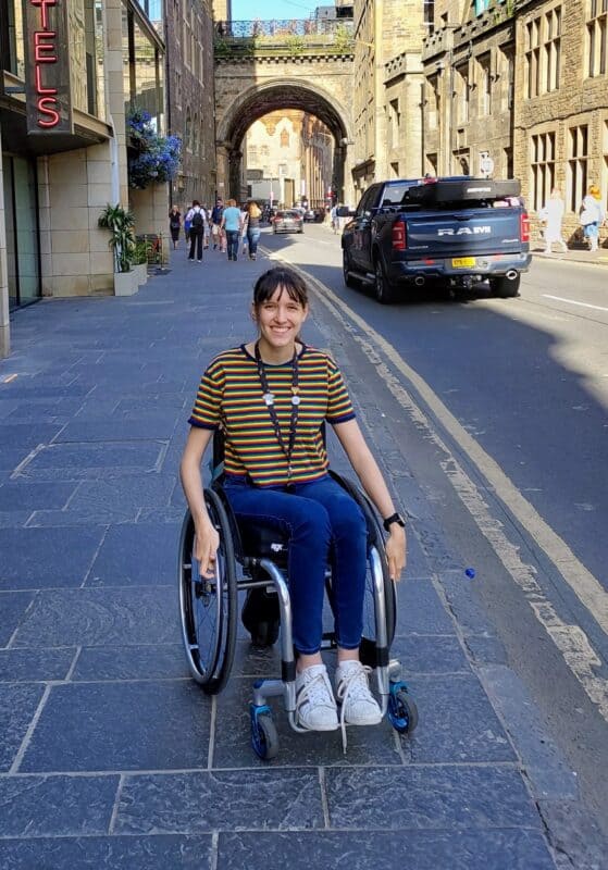 A young woman is smiling as she travels down an empty street in her wheelchair.