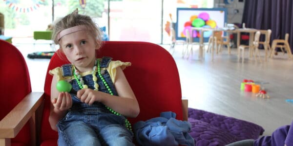Charlotte, a young girl wearing dungarees, sitting in the Sense TouchBase Pears playroom holding a maraca.
