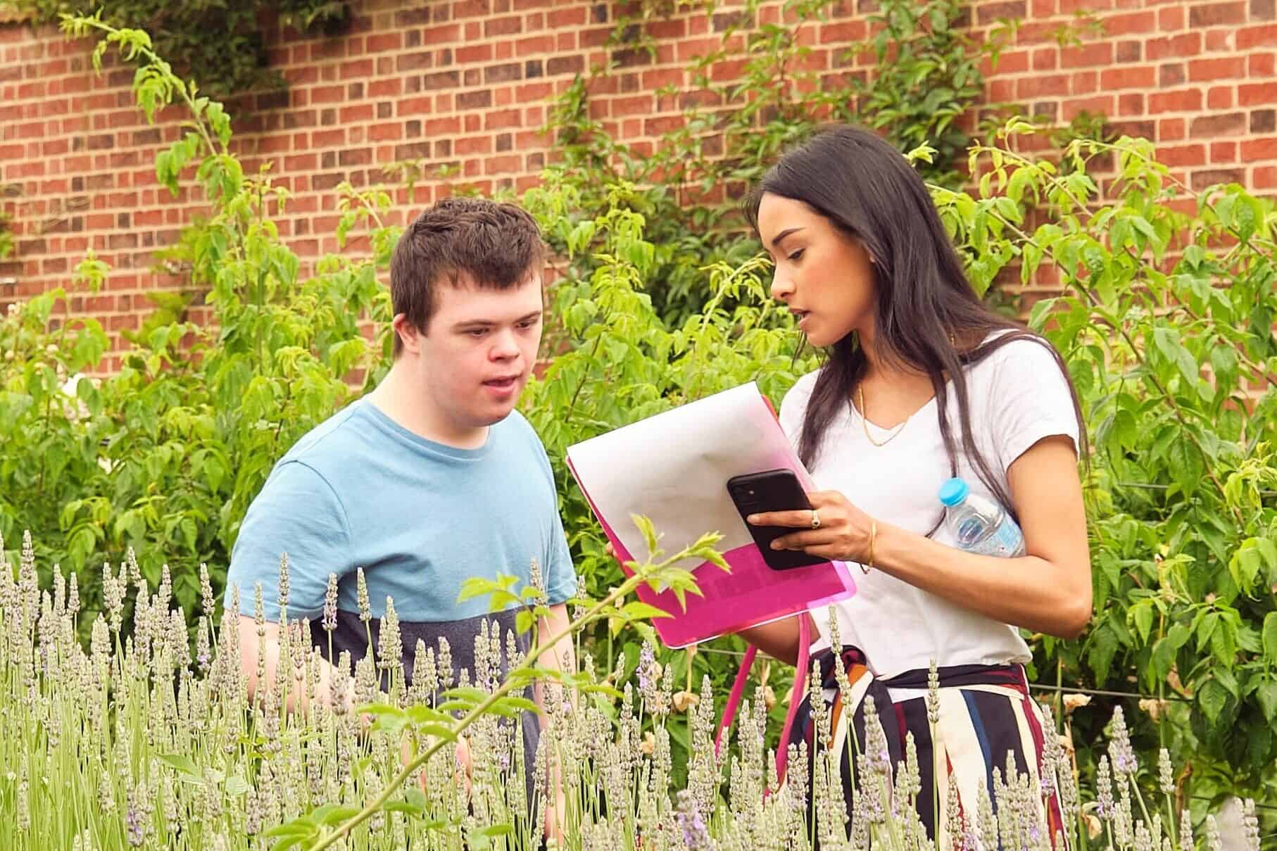A boy and a woman stand in a garden near some wildflowers