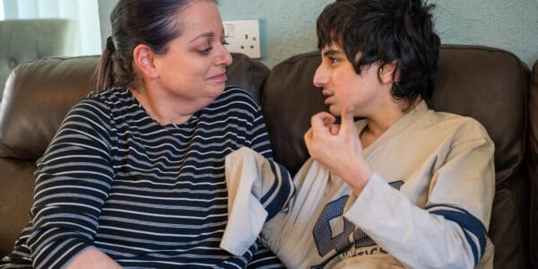 Sandra and Ayman are sitting facing each other. Ayman is using hand gestures to communicate with his mum