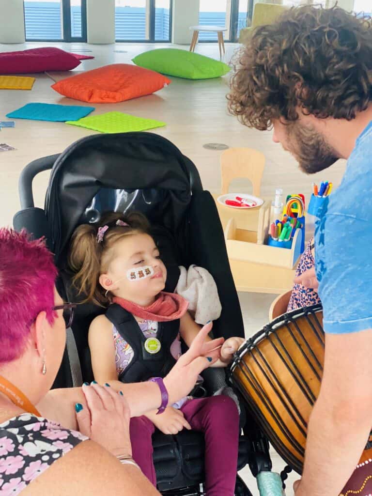 Verity tries playing a bongo drum, with the help of her support worker, Anne.