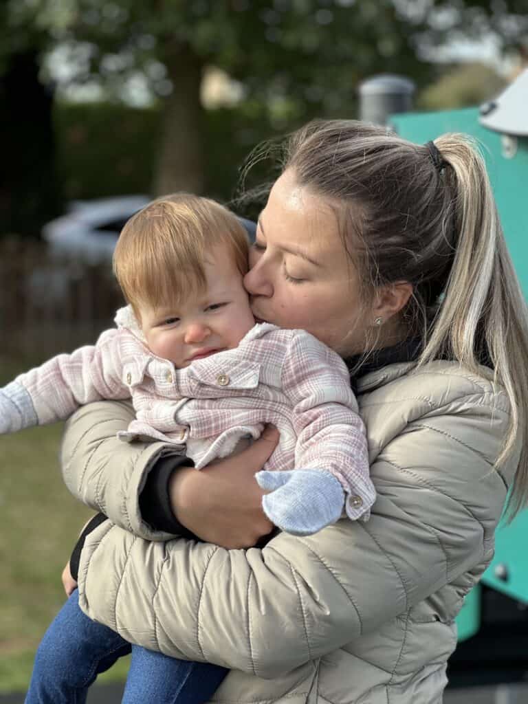 A woman hugging a young child and giving her a kiss on the back of her head