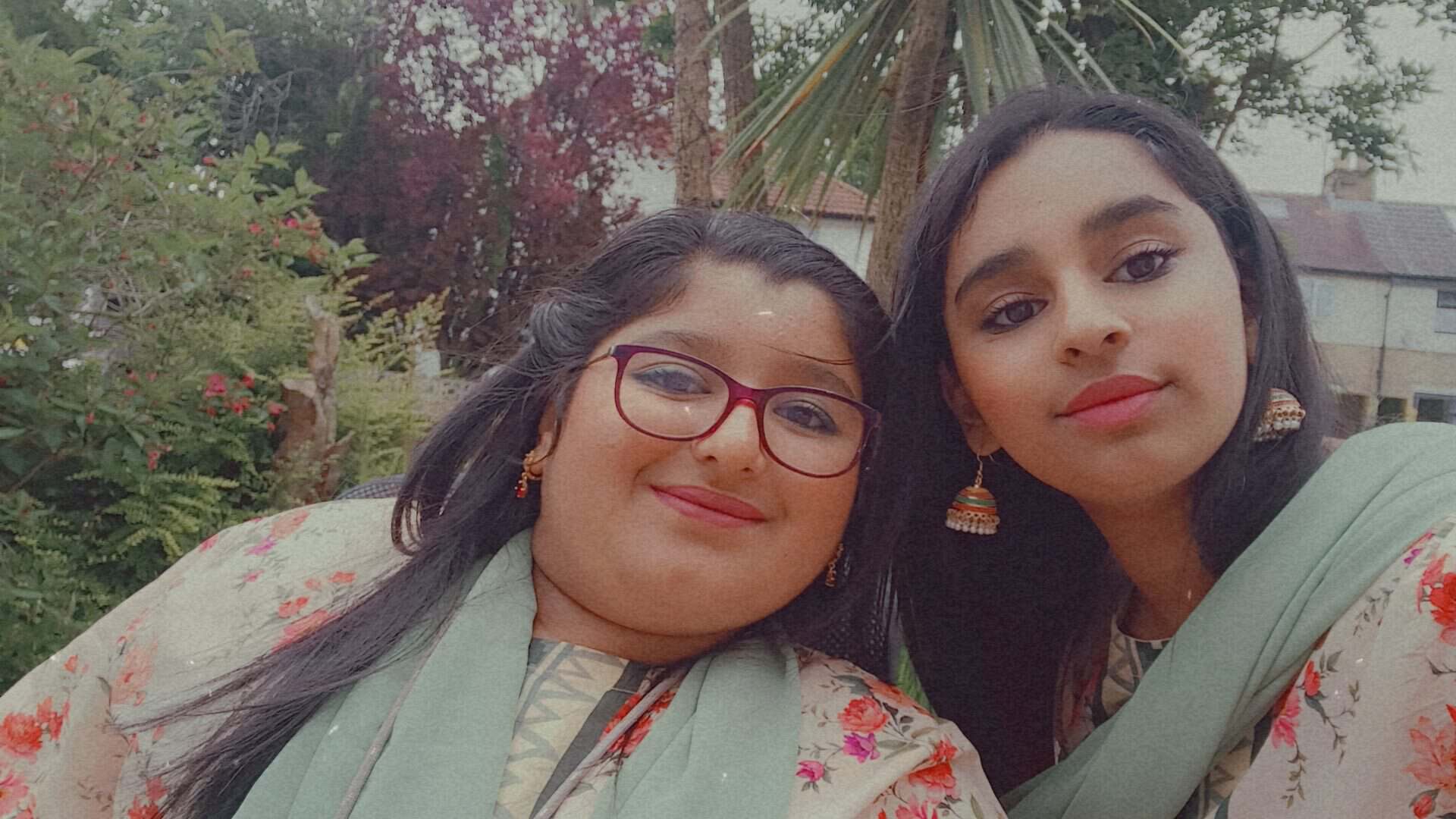 Two girls taking a selfie together outside in a garden. They are wearing South Asian clothes.