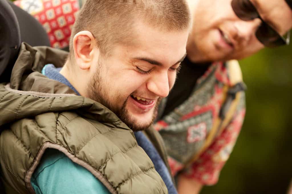 Archie is smiling with his face pointed away from someone standing behind him. He's got a beard and short brown hair.