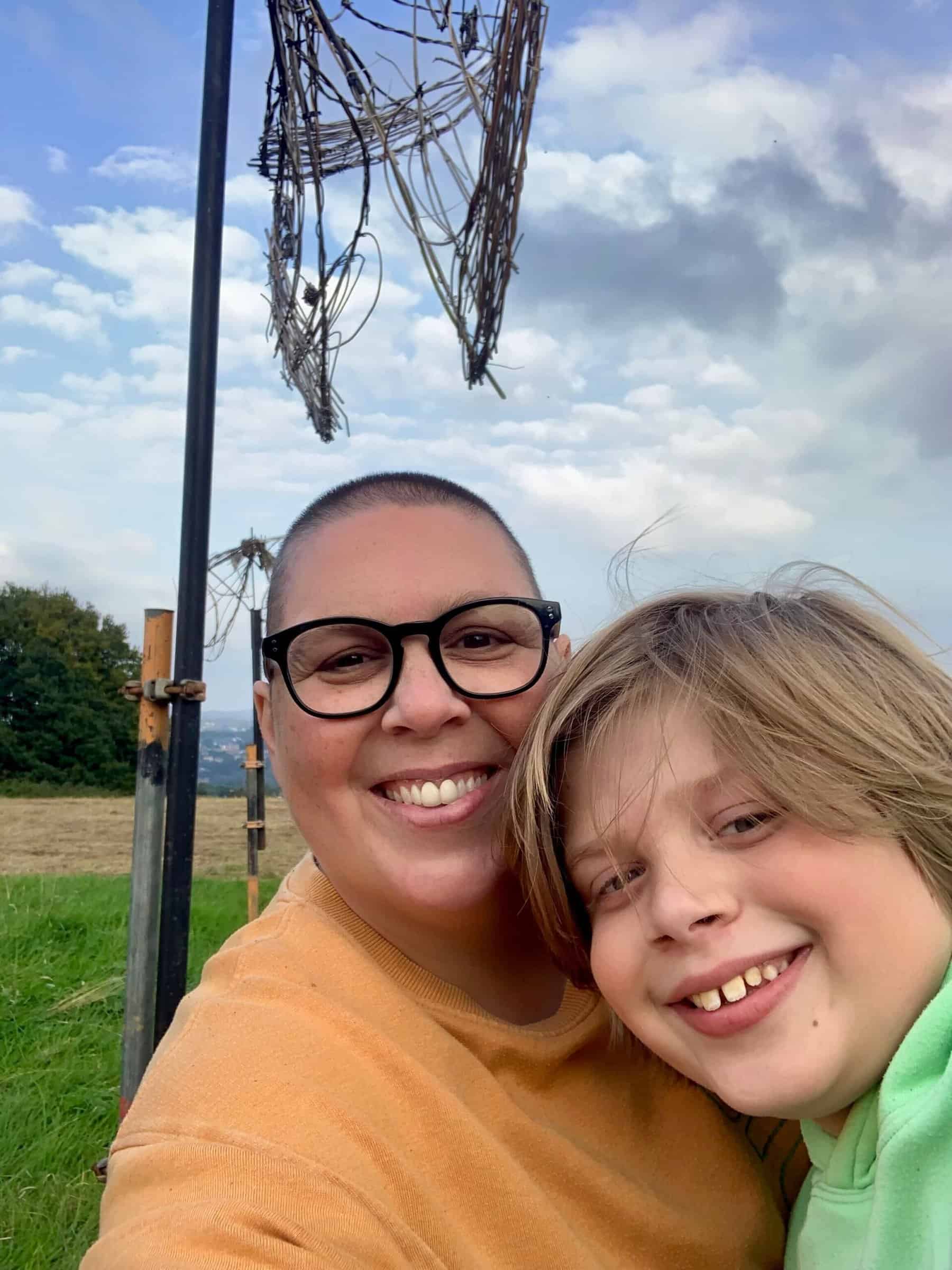 An adult and child are giving big smiles to the camera. They are outside and appear to be up a hill.