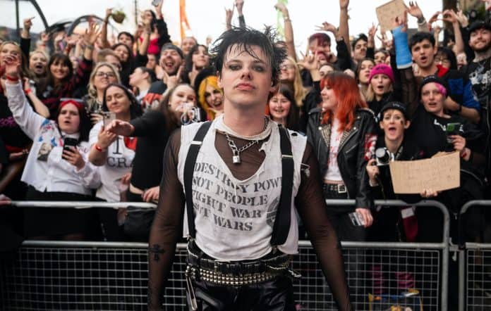 A man wearing gothic clothes stands in front of a crowd of fans.
