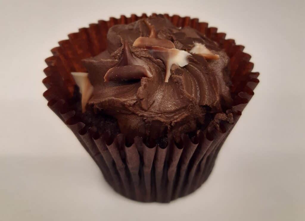 A picture of a chocolate cupcake, with chocolate flakes and icing on top. It has a dark brown wrapper around its bottom half.