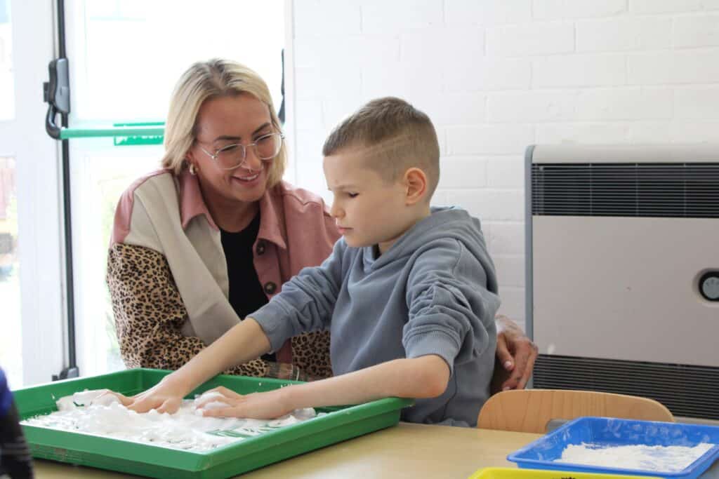 A boy playing with flour sitting next to his mum.