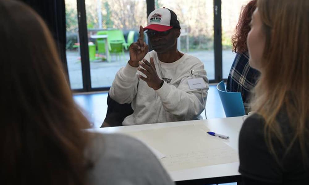 Kanhai, a deafblind man and a member of Sense User Reference Group, is using sign language to talk about his experience of social care to members of the Casey Commission on Adult Social Care.