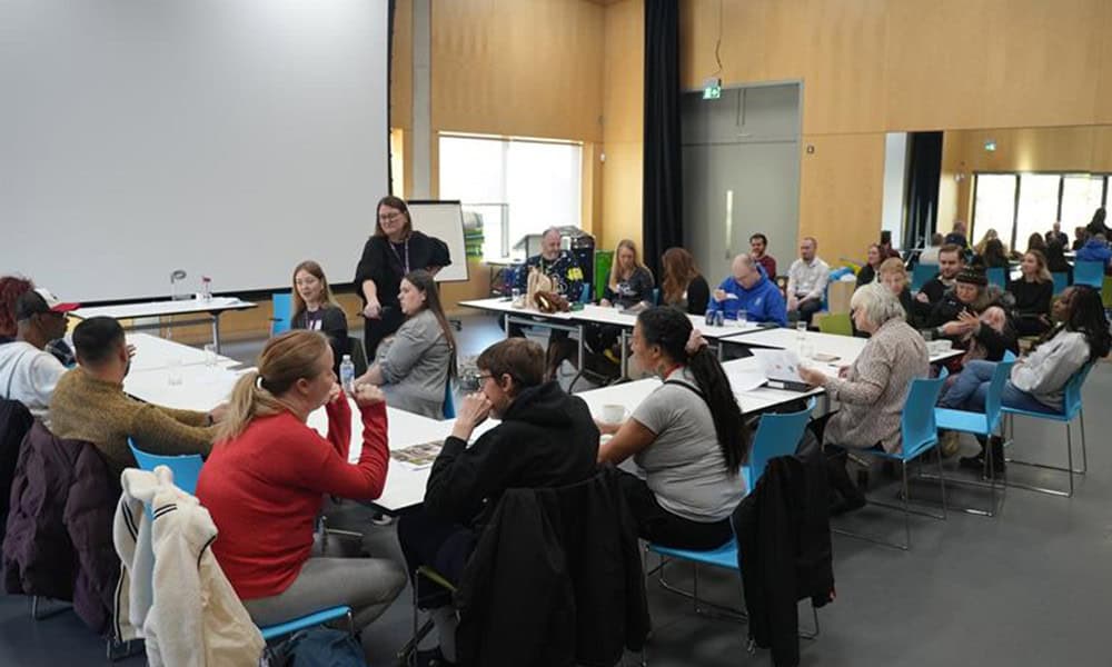 A meeting room in Sense TouchBase Pears, with tables set up in a horseshoe shape, with people sitting around a table talking to members of the Casey Commission on Adult Social Care.