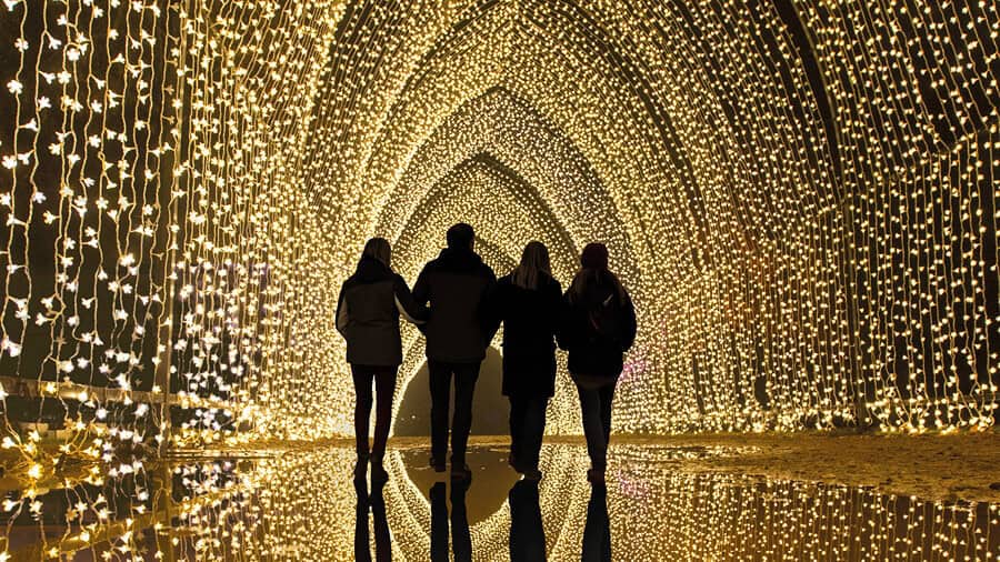 4 people walking through a tunnel of white lights