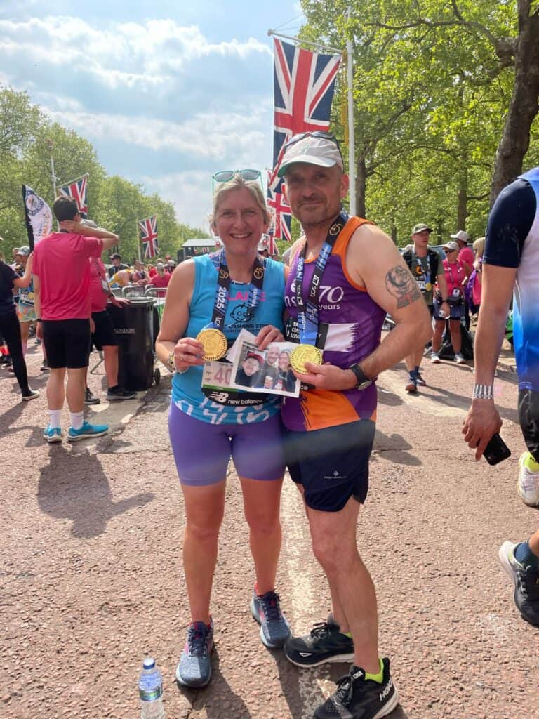 Two people at the finish line of the London Marathon. They are wearing their medals and holding up a photo of them with a child.