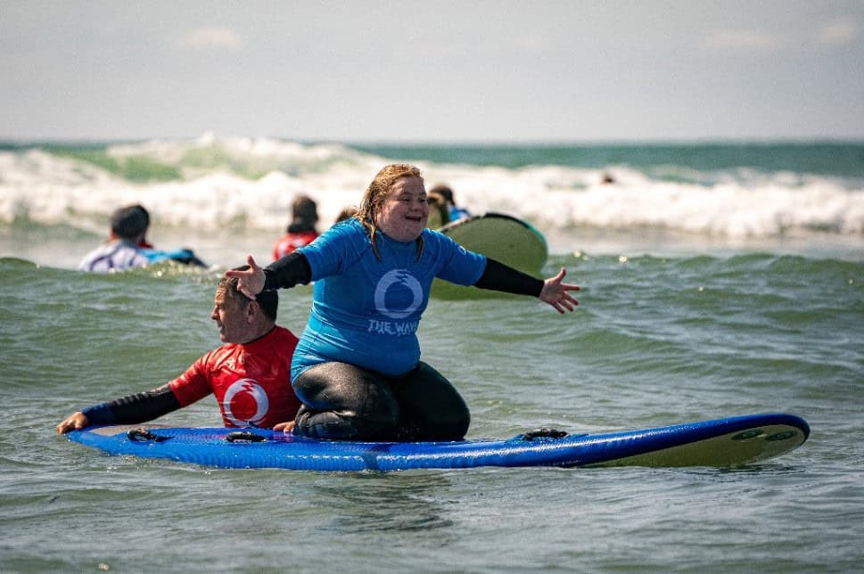 A woman wearing a blue shirt needs on a surfboard in the water