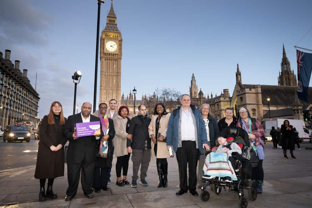 A group of people standing, and one sitting in a wheelchair, in front of Big Ben.