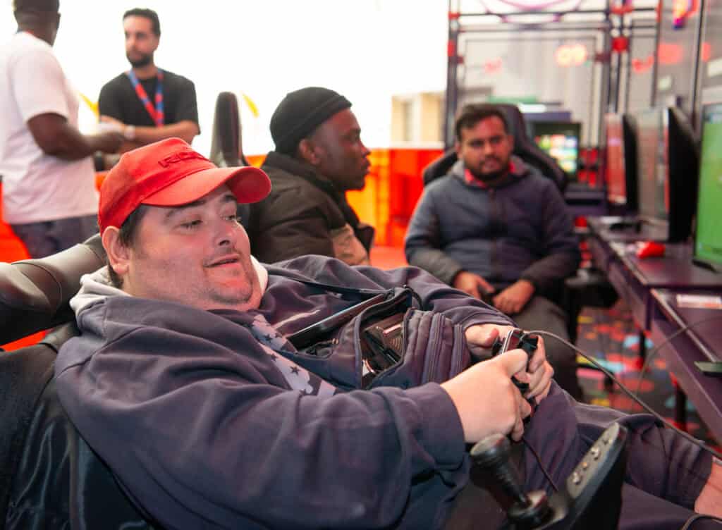 A man playing a game in an arcade. He is wearing an orange cap.