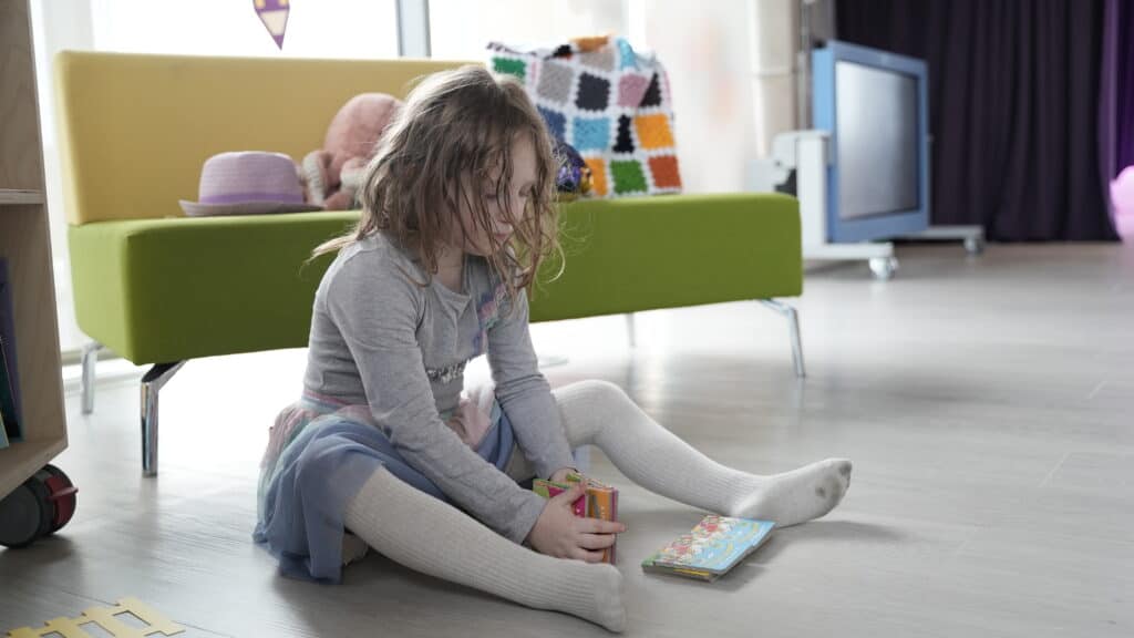 A young girl with long hair sits on the floor holding some small books.