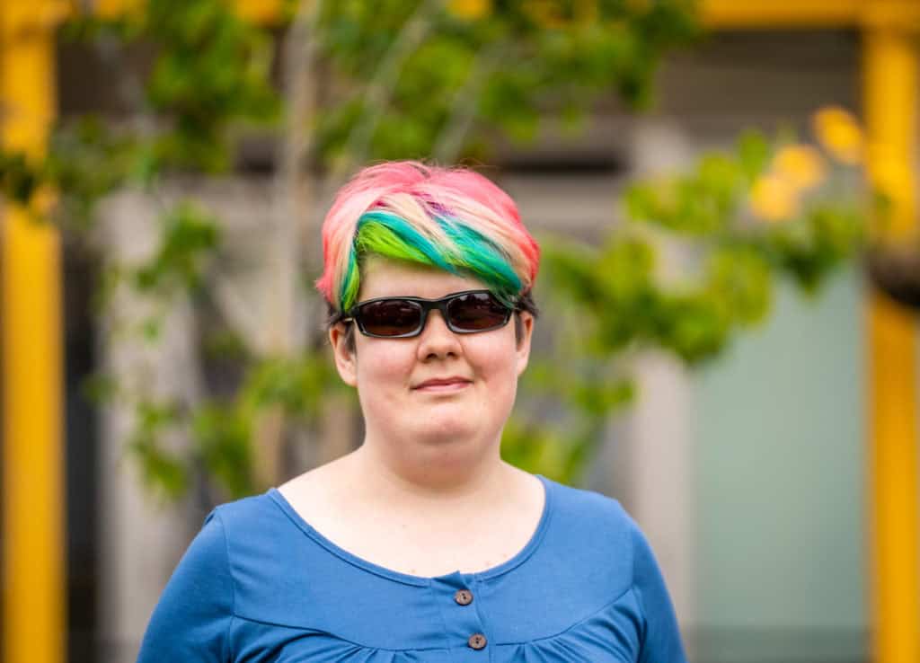 Lucy Dawson, a white woman with short, multi-coloured hair, who is wearing sunglasses.