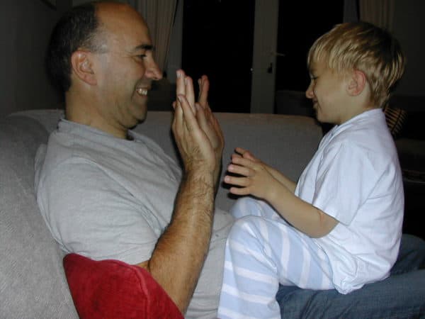 a child sits on his dads lap, facing him and looking at his hands
