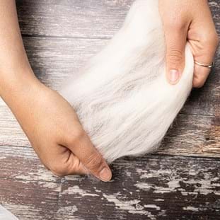 Image shows hands teasing out some of the white merino.