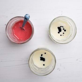 Three pots of finger paint being made, one is red and the other two are still pale with drops of paint in them
