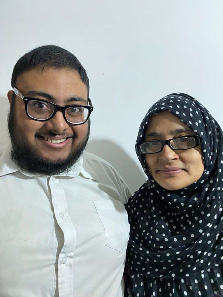 Saihan, a young man in glasses, with his mum Firdush, a woman wearing glasses and a hijab, both smiling to camera.