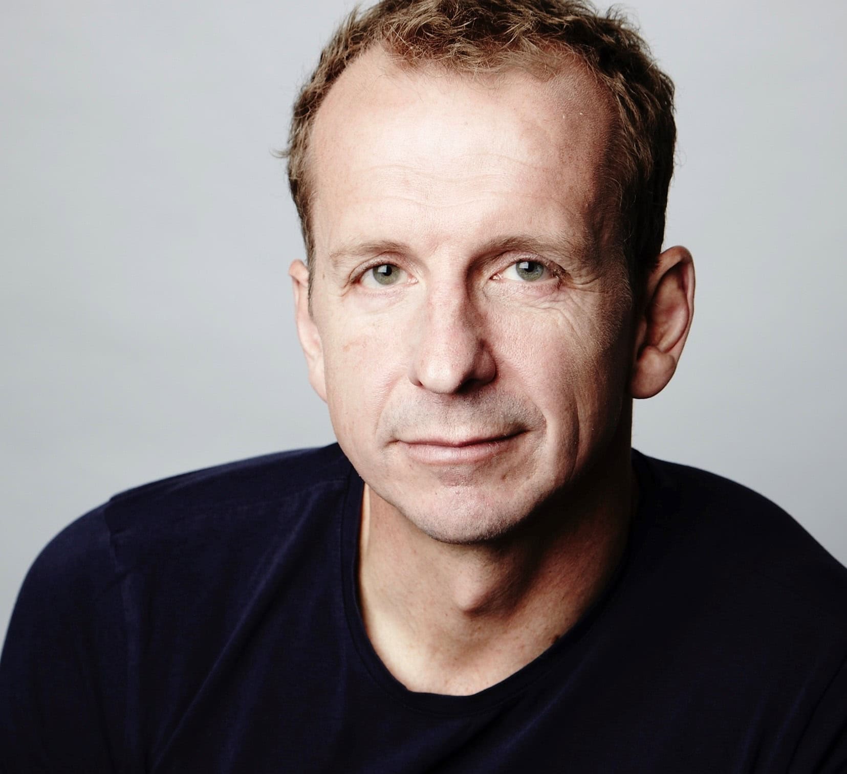 A portrait of a man with short hair and wearing a black shirt looking into the camera.
