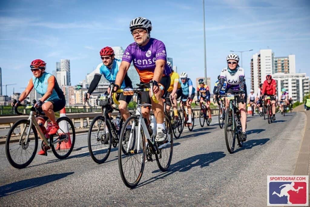 Guni Suri, in a Sense shirt and helmet, cycling in a sponsored ride surrounded by other cyclists.
