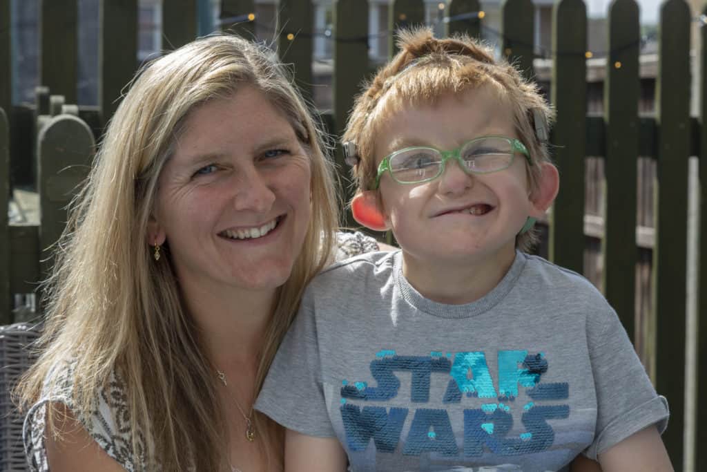 Hugo and his mum Claire smile for the camera. His mum has long blonde hair, and Hugo has blue glasses and a Stars Wars t-shirt