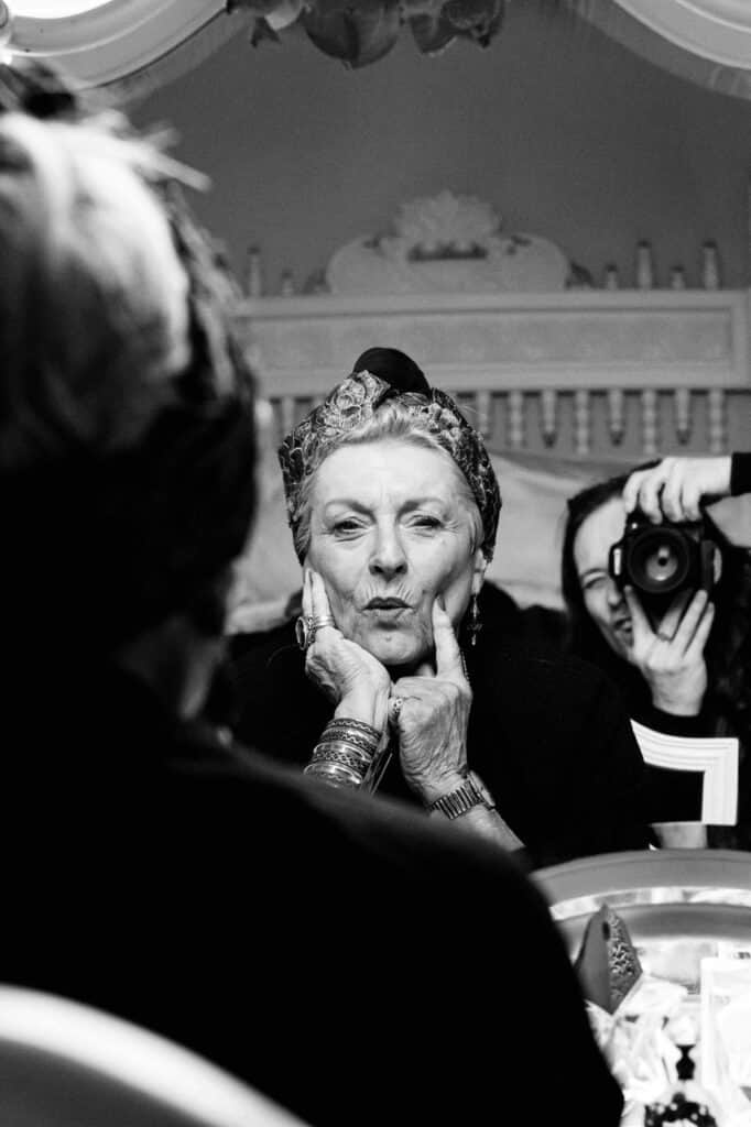 A woman pulls a face in the mirror, while a long-haired man behind her takes her photo. Photo by Ian Treherne.