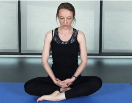 a woman sitting cross-legged on a mat with her hands in her lap