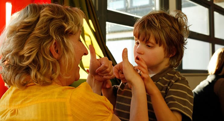 A woman is giving a young boy the thumbs up - she's smiling and he's looking at her hands