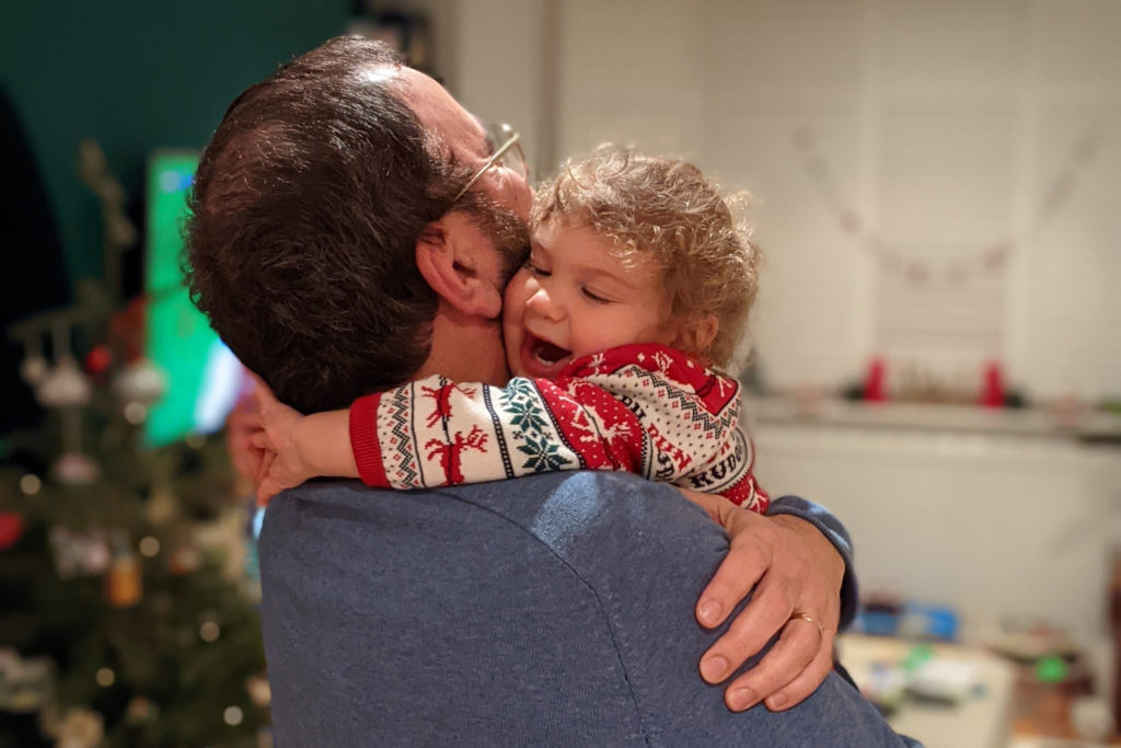 A man holds a small girl. The girl has her arms around the man's neck. Her mouth is open with delight and her eyes are closed.
