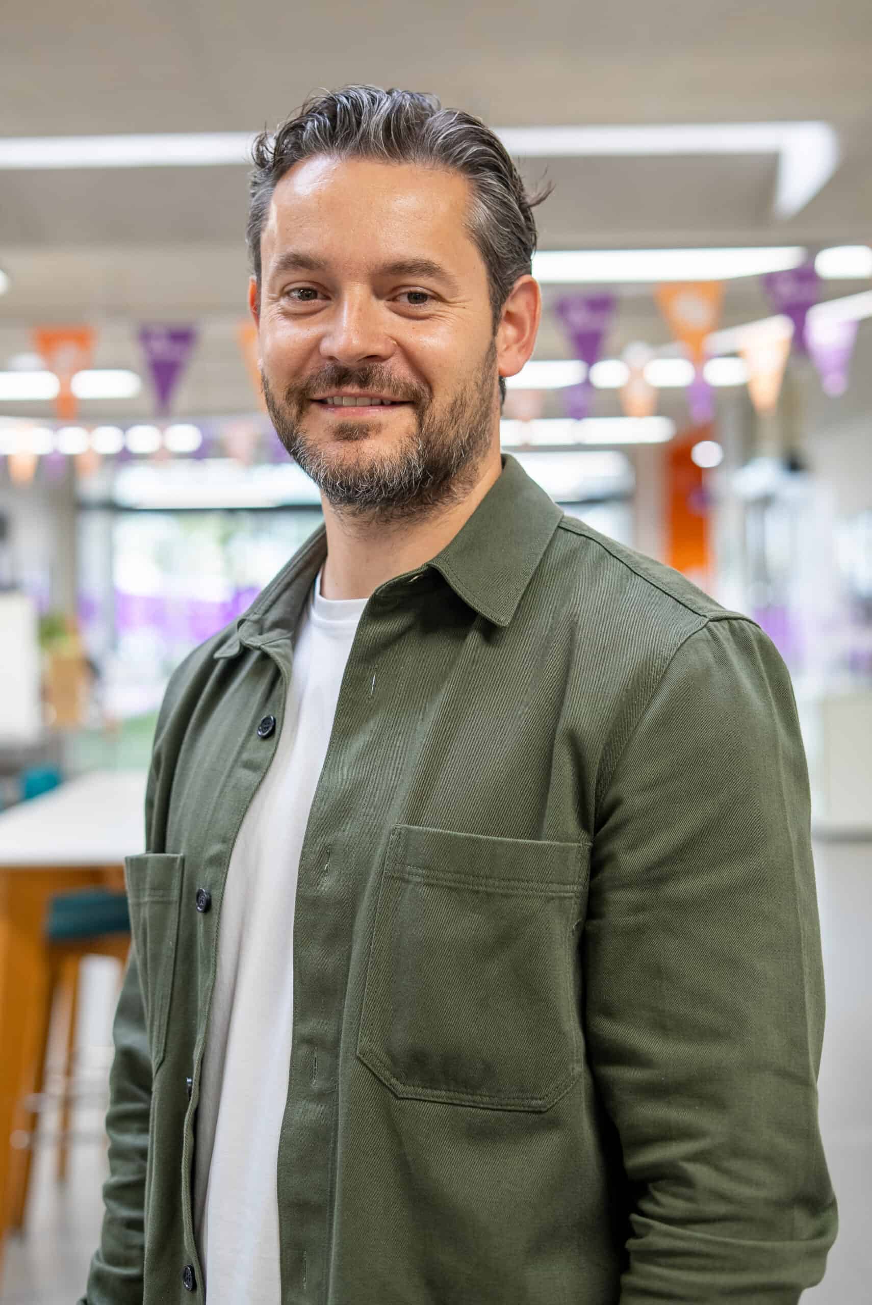 A portrait of a man smiling and wearing a green shacket.
