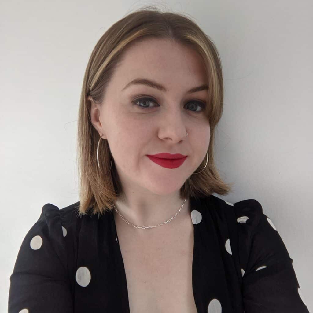 A headshot of a person wearing red lipstick and a black and white spotted top.