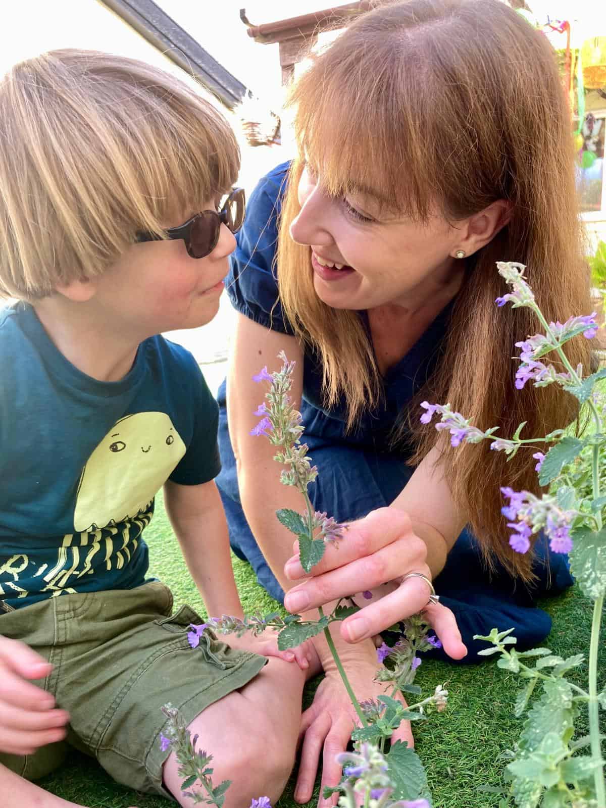A woman in a garden with a young boy. She is showing him a plant.