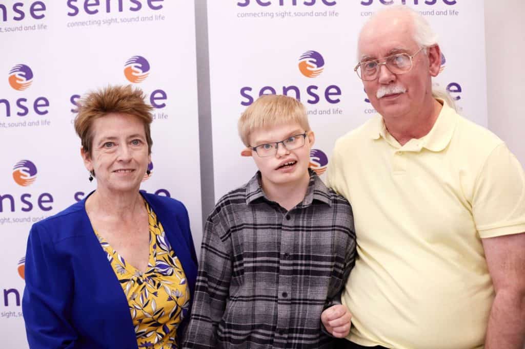 Three people smiling at the camera. On the left is a woman, in the middle a young man, and on the right another man.
