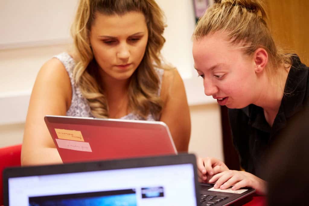 A young woman with blonde hair being supported to use a computer.