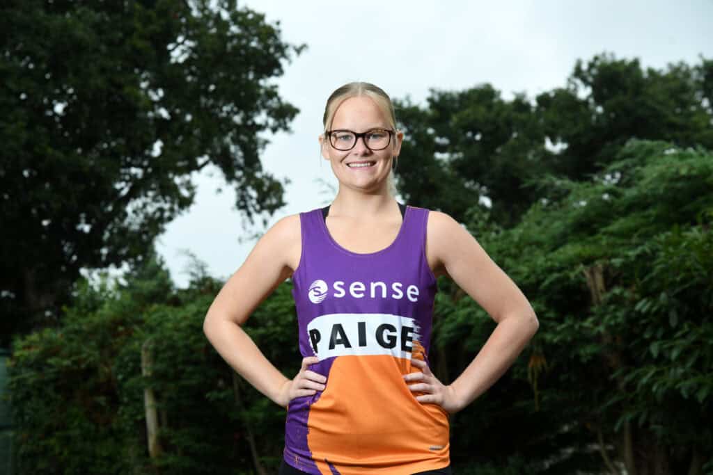 A young woman stands with her hands on hips, wearing her Sense marathon vest.