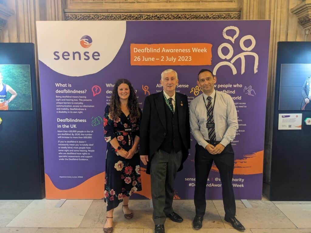 Three people standing in front of an exhibition smiling at the camera. One of them is the speaker of the house of commons.