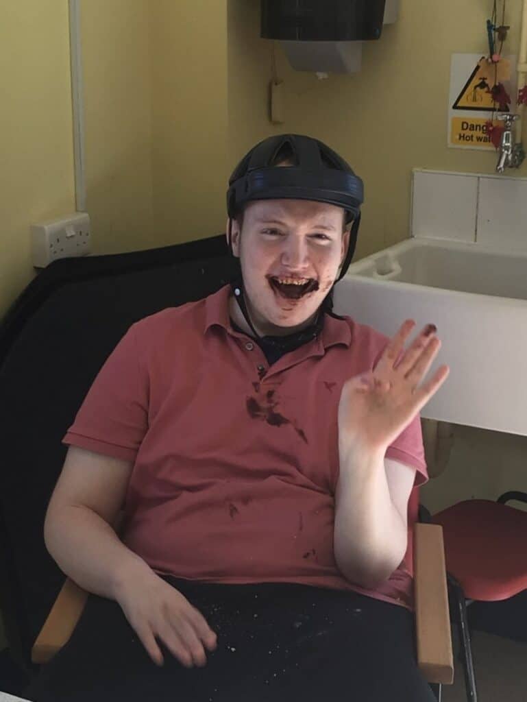 Luke, a boy wearing a helmet, laughing with some chocolate around his mouth.