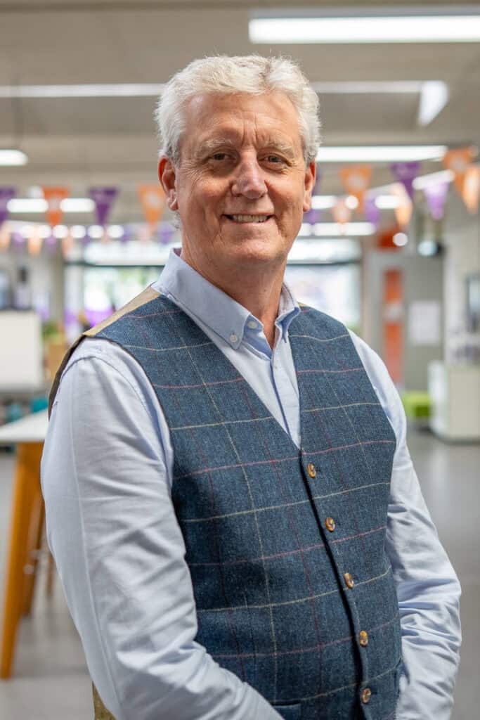 A portrait of a man wearing a blue shirt and paterned waistcoat.
