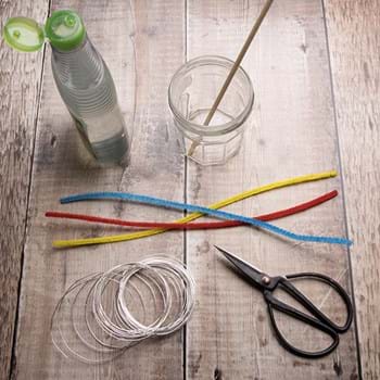 Red, yellow and blue pipe cleaners, some spools of wire, scissors, an empty jar and washing-up liquid