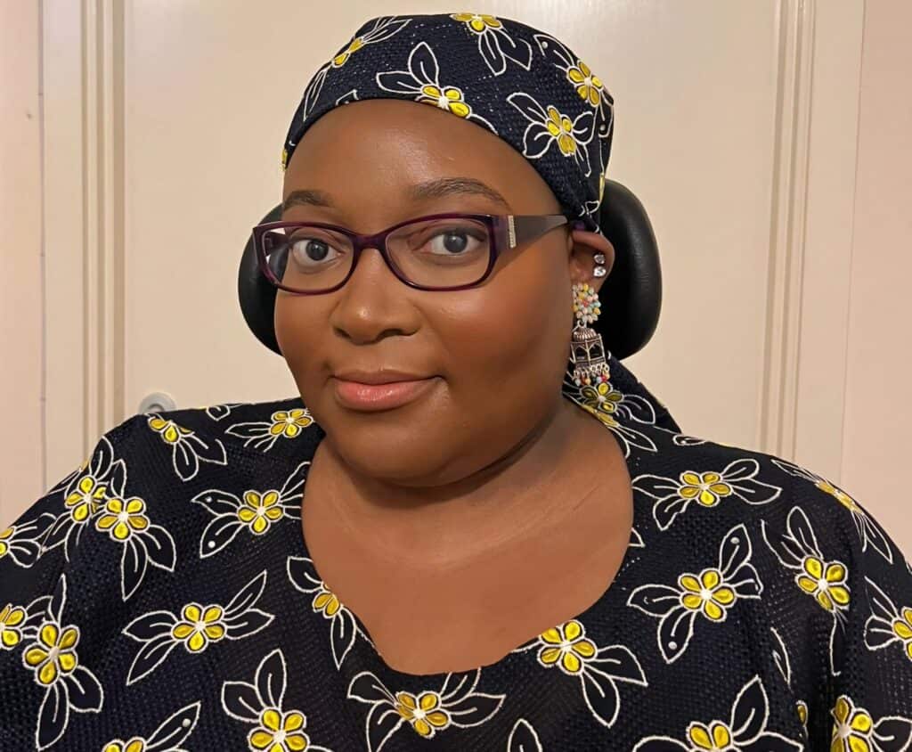 Matilda Feyisayo Ibini, a Black woman wearing a black and yellow floral top and matching headscarf.