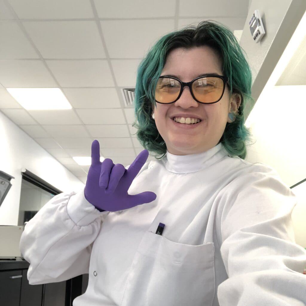 A person green highlights in their hair wearing a lab coat 